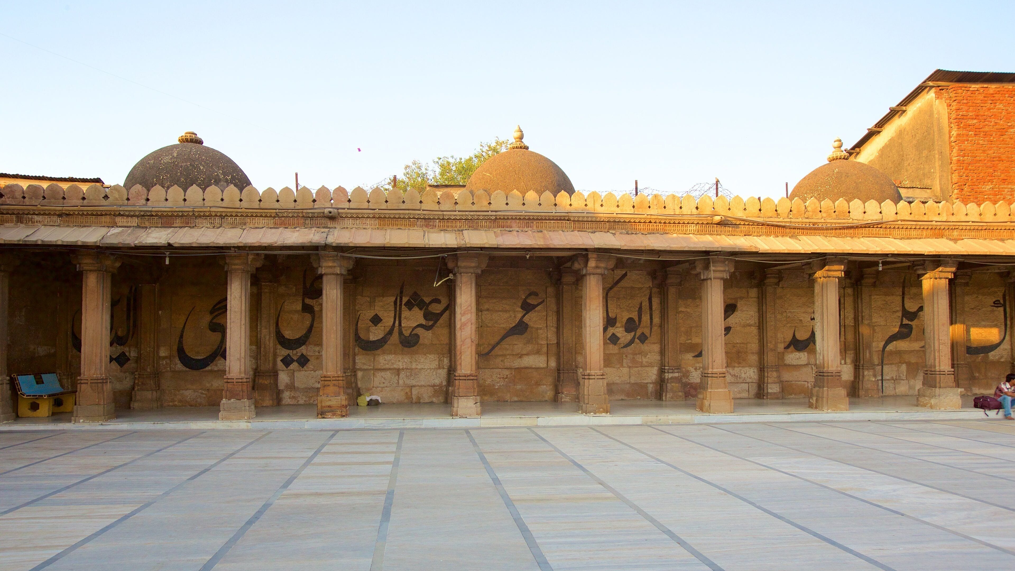 A courtyard with a row of arches and columns, featuring Arabic calligraphy.