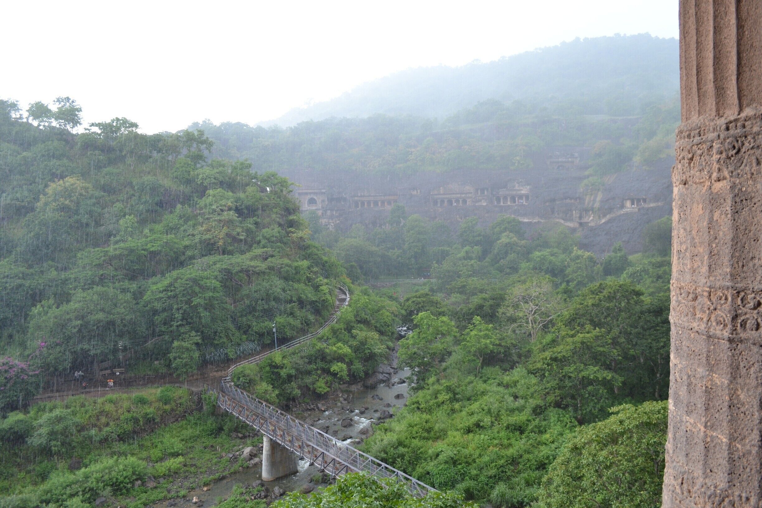 A bridge over a river surrounded by dense forest and ancient ruins in the background.