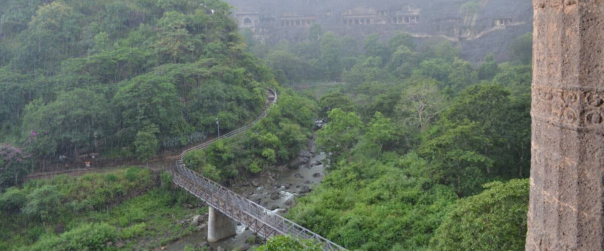 A bridge over a river surrounded by dense forest and ancient ruins in the background.