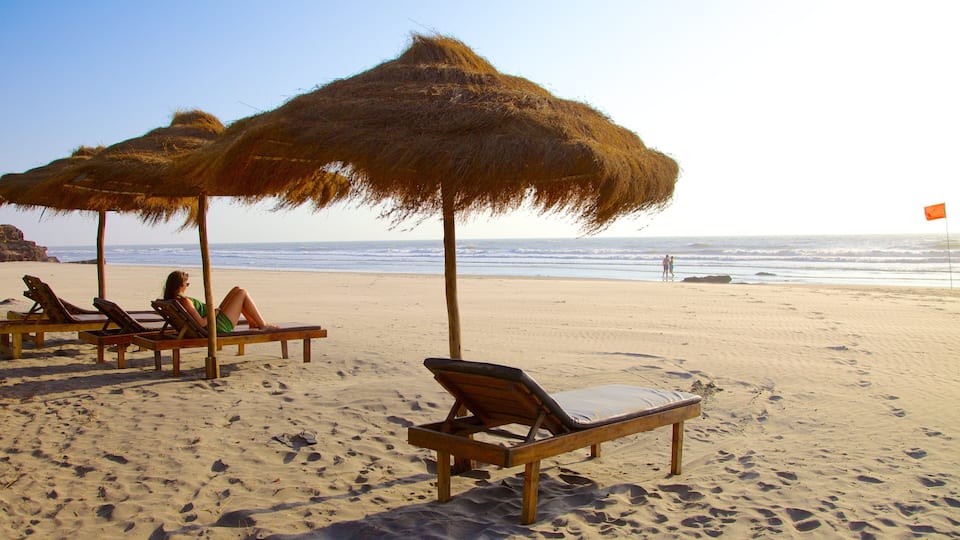 A beach with thatched umbrellas, lounge chairs, and footprints in the sand.
