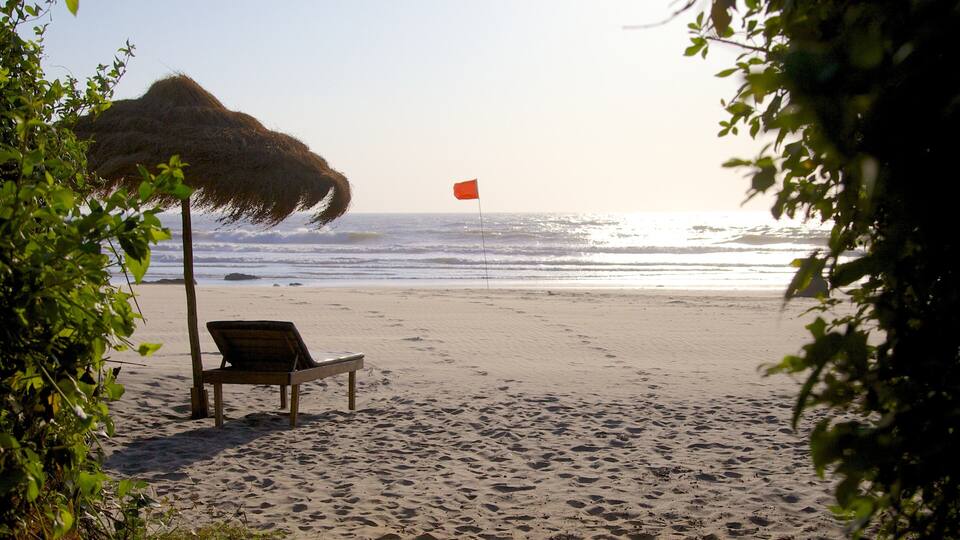A beach with a chair and a thatched umbrella, a flag in the distance, and the ocean.