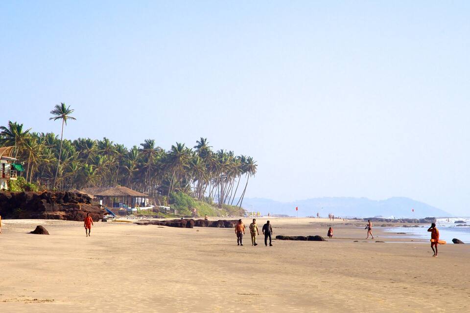 A beach with palm trees, a lifeguard tower, and people walking.