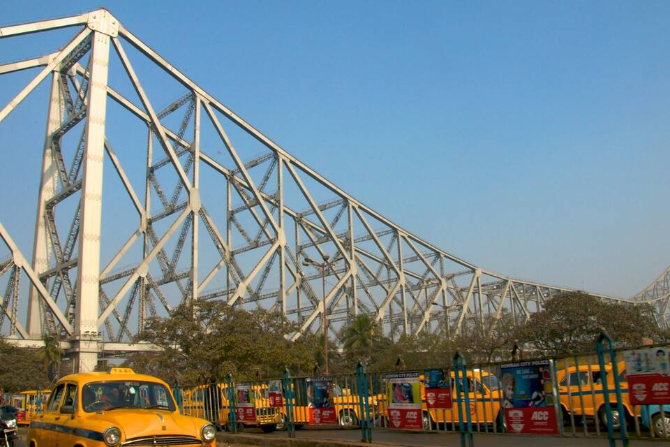 A large steel bridge with yellow taxis and buses in the foreground.