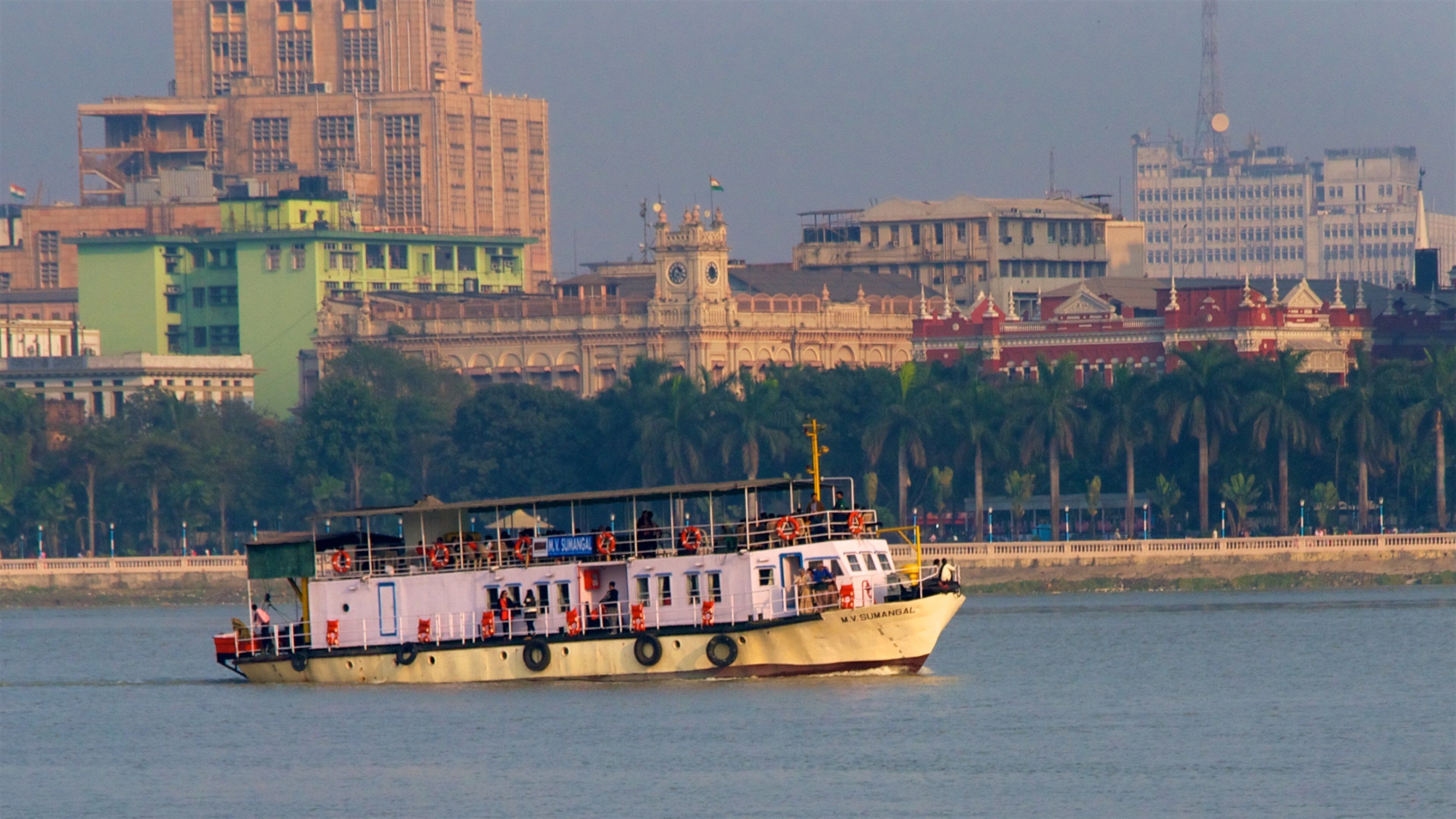 A ferry boat on a river with a cityscape in the background.