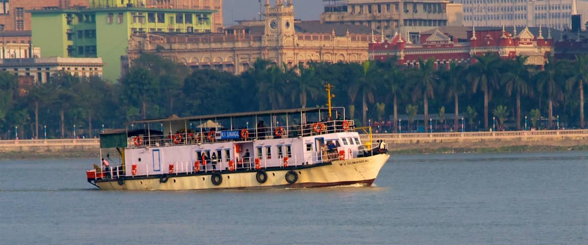 A ferry boat on a river with a cityscape in the background.
