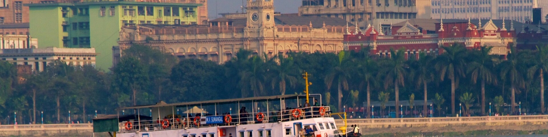 A ferry boat on a river with a cityscape in the background.