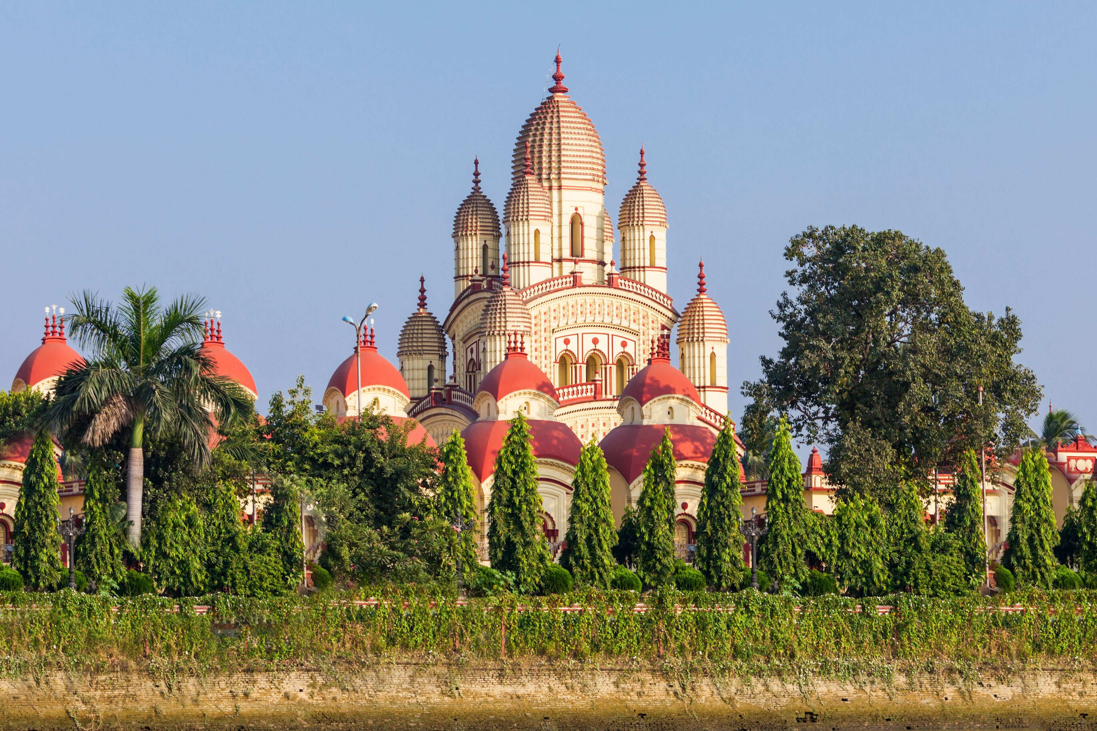 A large, multi-domed building with red and white domes, surrounded by greenery and palm trees.