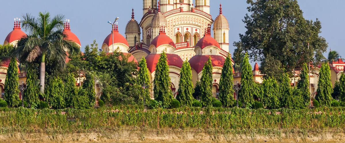 A large, multi-domed building with red and white domes, surrounded by greenery and palm trees.