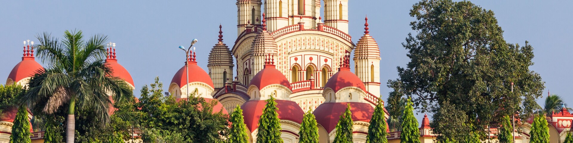 A large, multi-domed building with red and white domes, surrounded by greenery and palm trees.