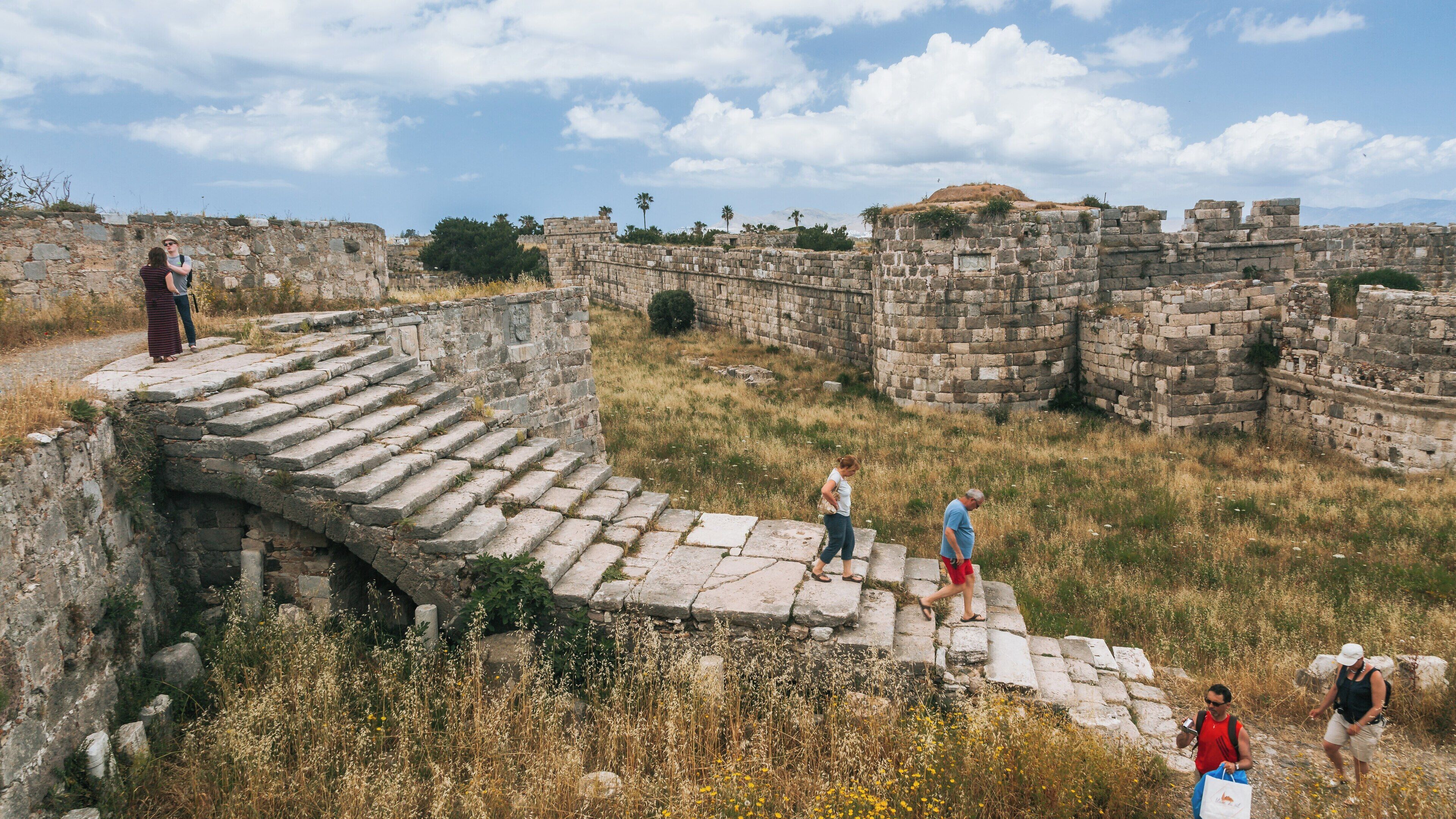 Exploring the ancient ruins of Kos Castle in South Aegean Greece under a bright blue sky with visitors encountering history