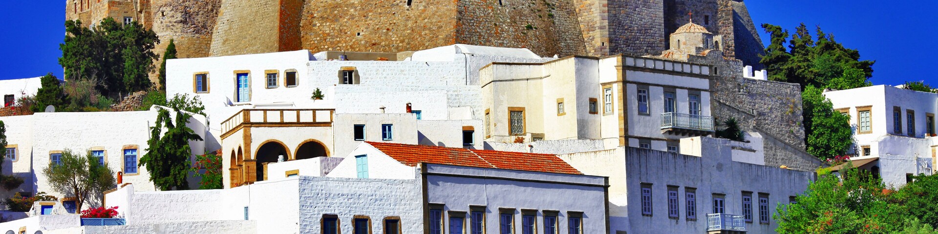 A historic castle atop a hill with white buildings in the foreground.
