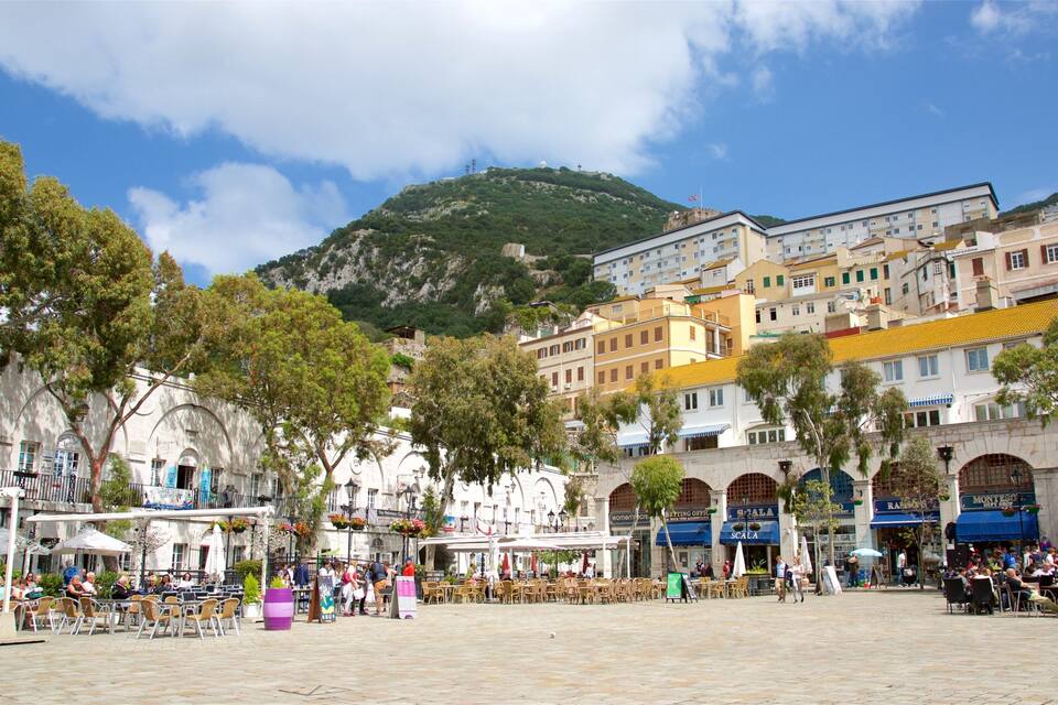 A bustling square with outdoor seating, surrounded by historic buildings and a mountain backdrop.