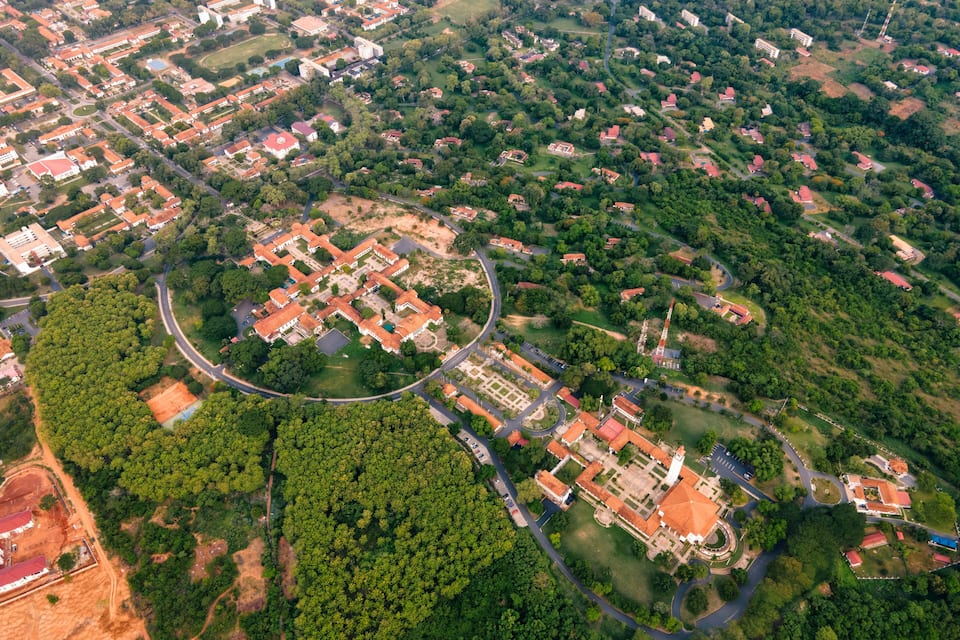 An aerial view of a town with a central square, surrounding buildings, and extensive greenery.