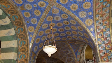 Een gedetailleerd plafond met ingewikkelde blauwe en gouden patronen, een hangend wit voorwerp en een mozaïekrand.