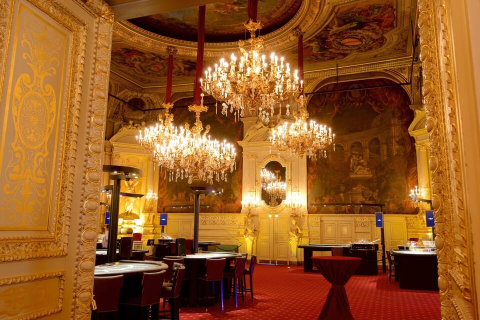 Een weelderig interieur met gedetailleerde gouden versieringen, kroonluchters en een vloer met een roodgeel tapijt.
