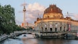 A historic building with a dome, a bridge over a river, and a tower in the background.