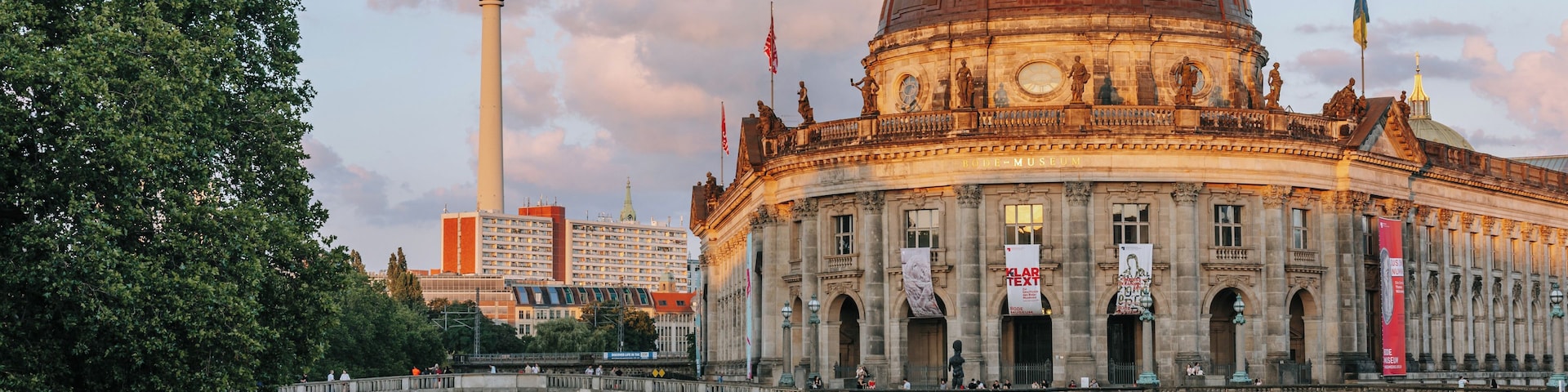 Um edifício histórico com uma cúpula, uma ponte sobre um rio e uma torre ao fundo.
