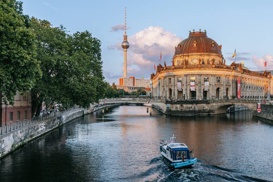 A river with a boat, a bridge, and a large historic building with a dome.