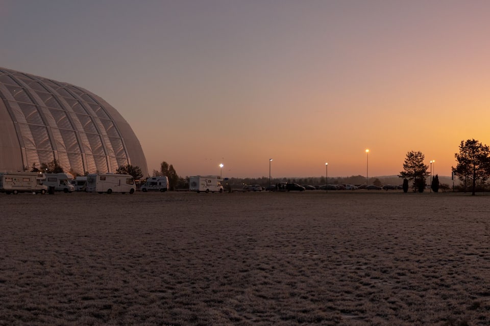 A large, dome-shaped building with a field of parked vehicles in front.
