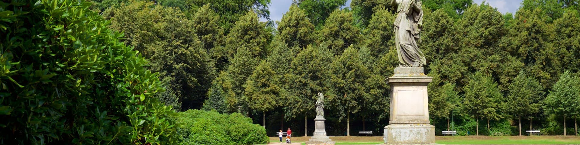 Un parc avec une statue, un étang et de nombreux arbres.