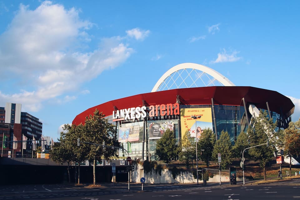 Een modern stadion met een grote koepel en een rood dak, omgeven door bomen en stadsgebouwen.