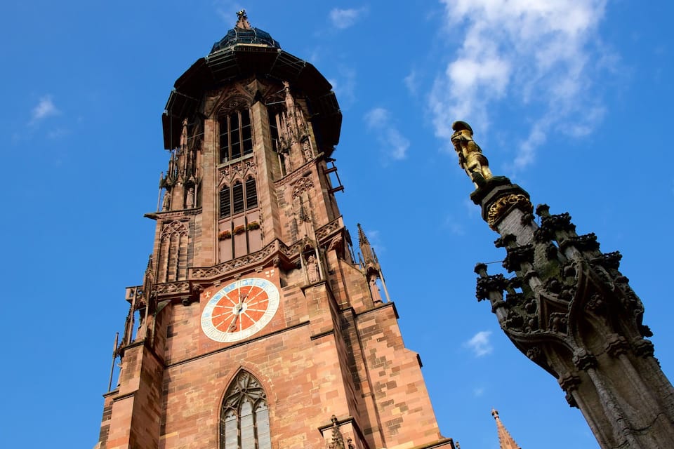 A tall church tower with a large clock and a statue on top.