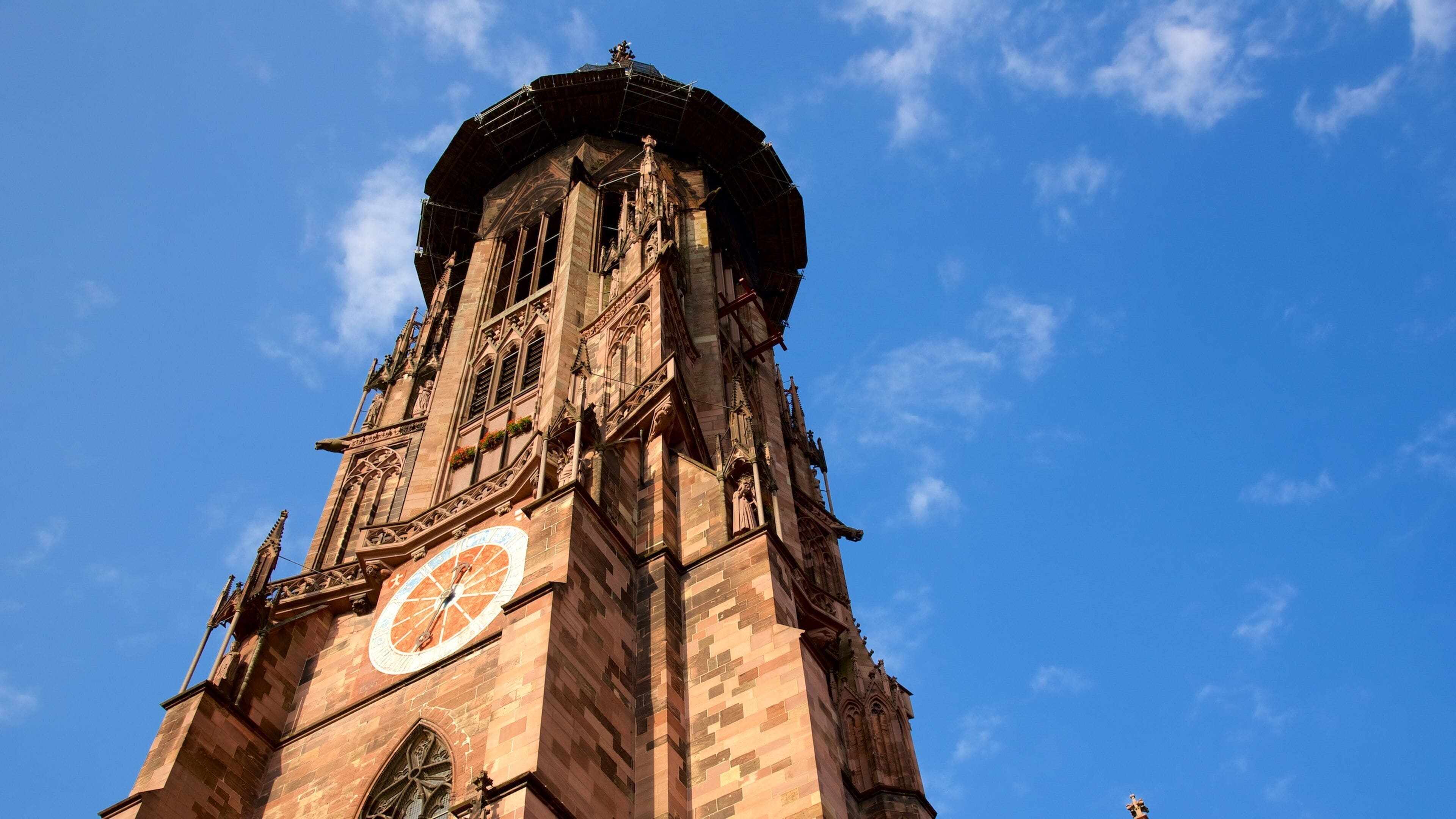 Una alta torre del reloj con detalles arquitectónicos intrincados y un cielo azul despejado al fondo.