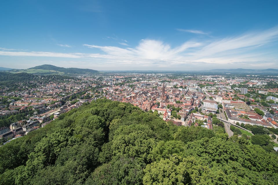 A city with a prominent church, surrounded by lush green hills and a clear blue sky.