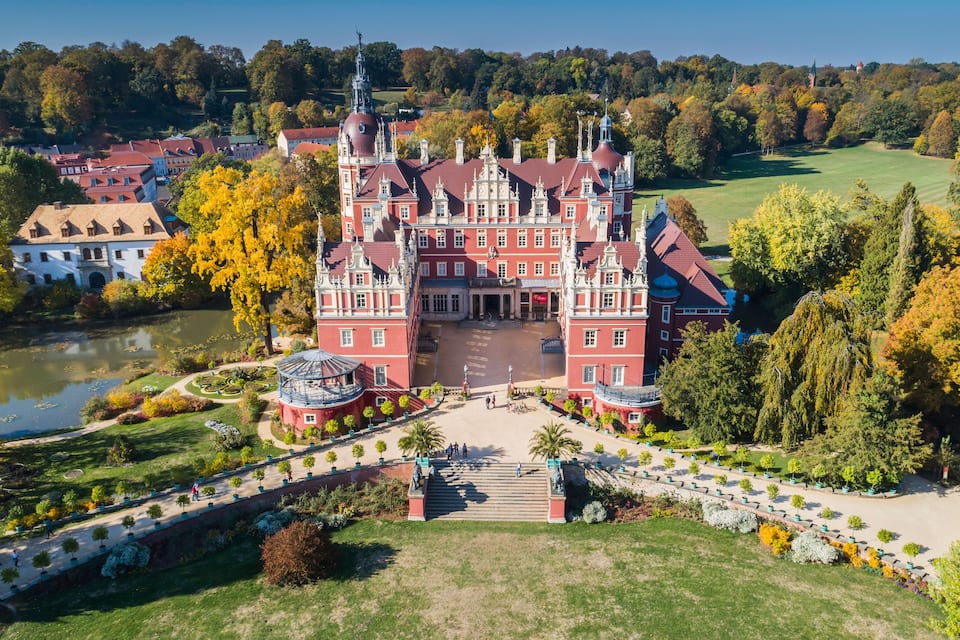A grand castle with a central courtyard, surrounded by lush gardens and a lake.