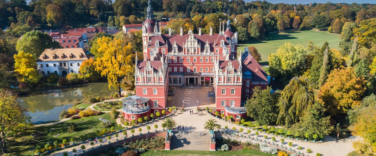 A grand castle with a central courtyard, surrounded by lush gardens and a lake.