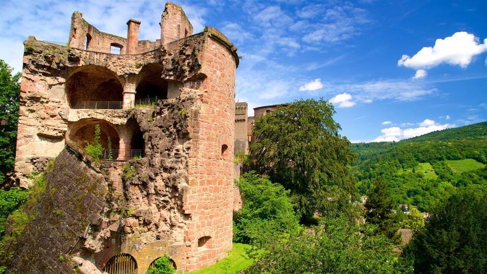A historic stone castle ruin surrounded by lush green hills and a clear blue sky.