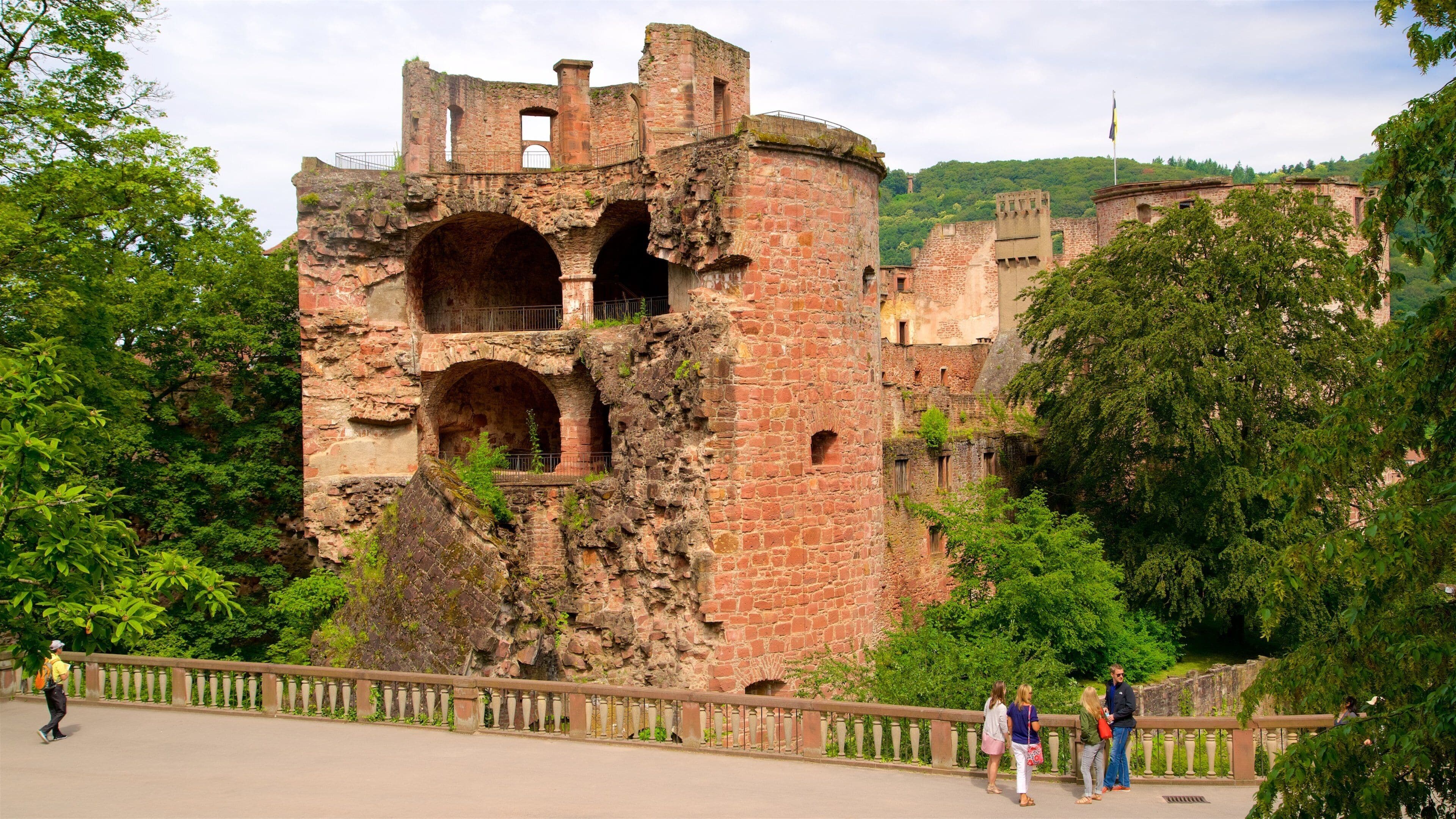 A historic stone tower with arched openings, surrounded by lush greenery and a paved walkway.