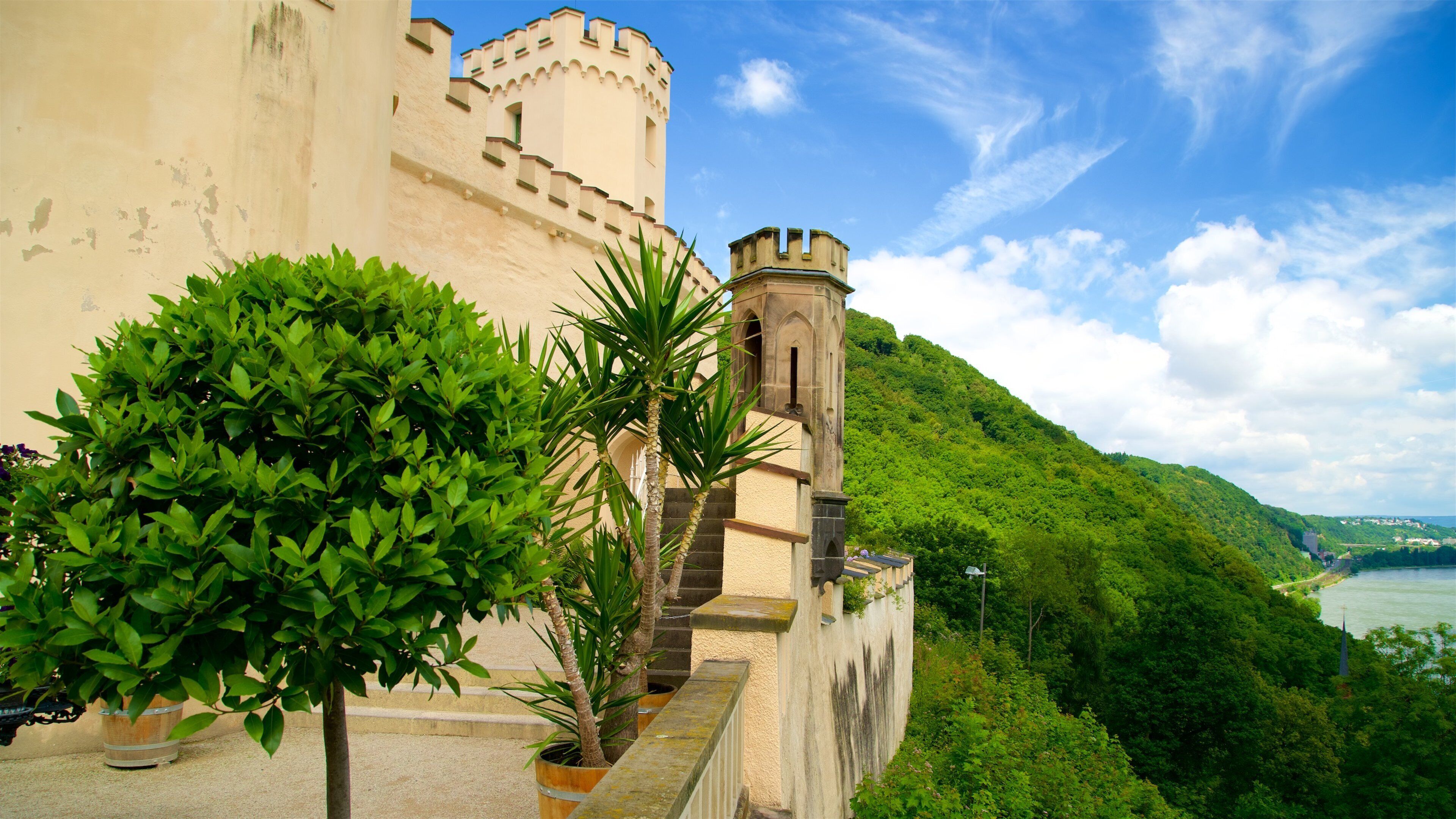 A castle with a tower, lush greenery, and a river.