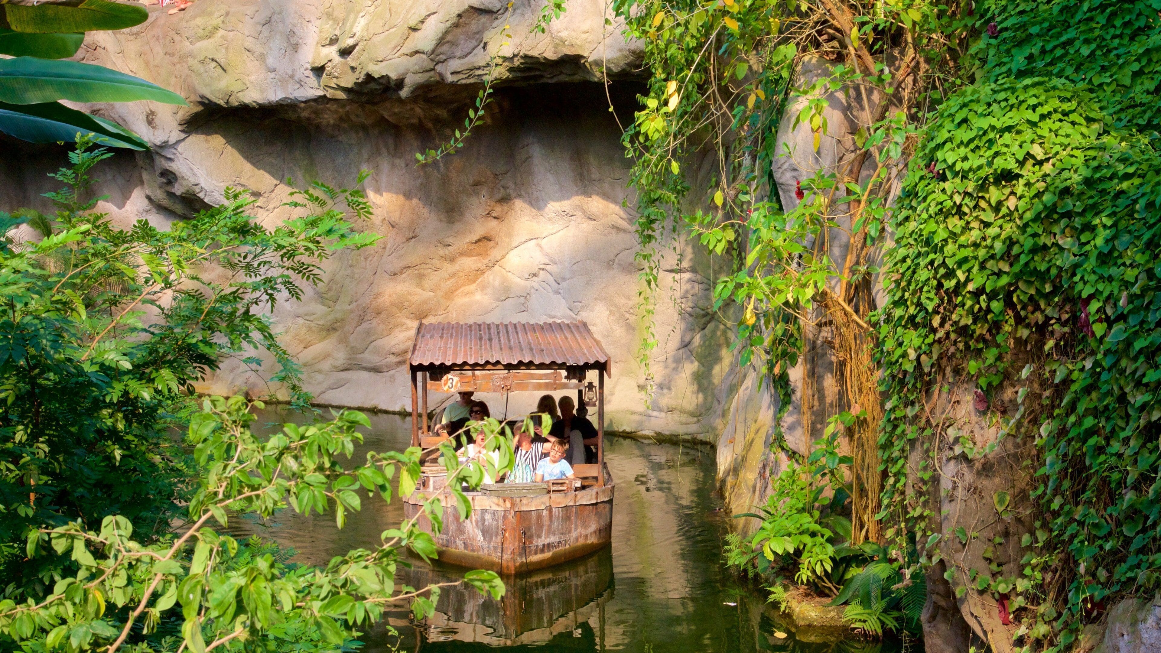 A boat with people on a river surrounded by greenery and a rocky cave.