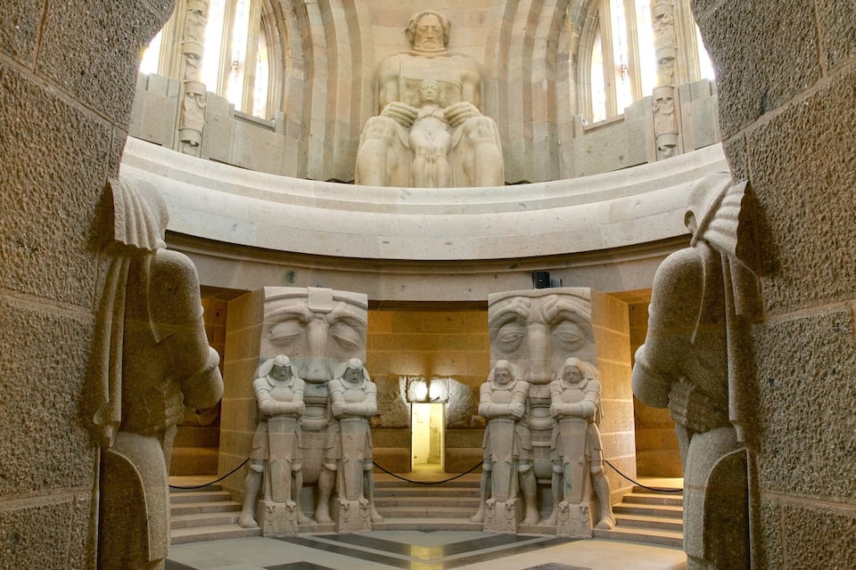 A grand stone archway with statues on either side, leading to a high arched ceiling.