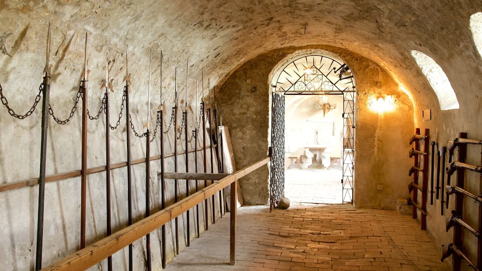 An arched stone corridor with wooden benches and metal racks holding spears and swords.