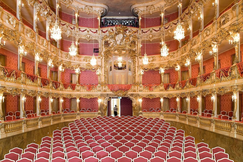 Un teatro sfarzoso con sedili rossi, decorazioni dorate e lampadari.