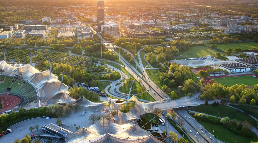 Modern European aerial cityscape with commercial and sports facilities, parks, multilane highway junction, tower blocks in outskirts illuminated by warm glowing sunlight at dusk Munchen Bayern Germany