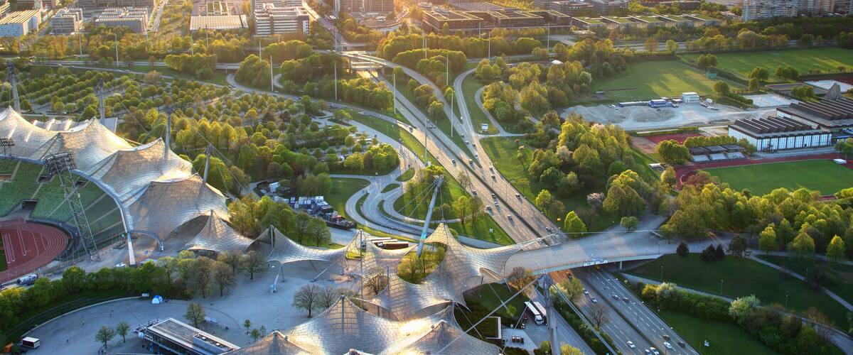 Modern European aerial cityscape with commercial and sports facilities, parks, multilane highway junction, tower blocks in outskirts illuminated by warm glowing sunlight at dusk Munchen Bayern Germany