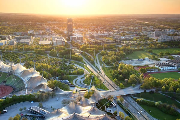 Modern European aerial cityscape with commercial and sports facilities, parks, multilane highway junction, tower blocks in outskirts illuminated by warm glowing sunlight at dusk Munchen Bayern Germany
