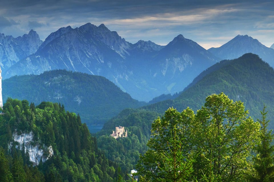 Eine Burg auf einem Berg, umgeben von dichten Wäldern und hoch aufragenden Gipfeln.