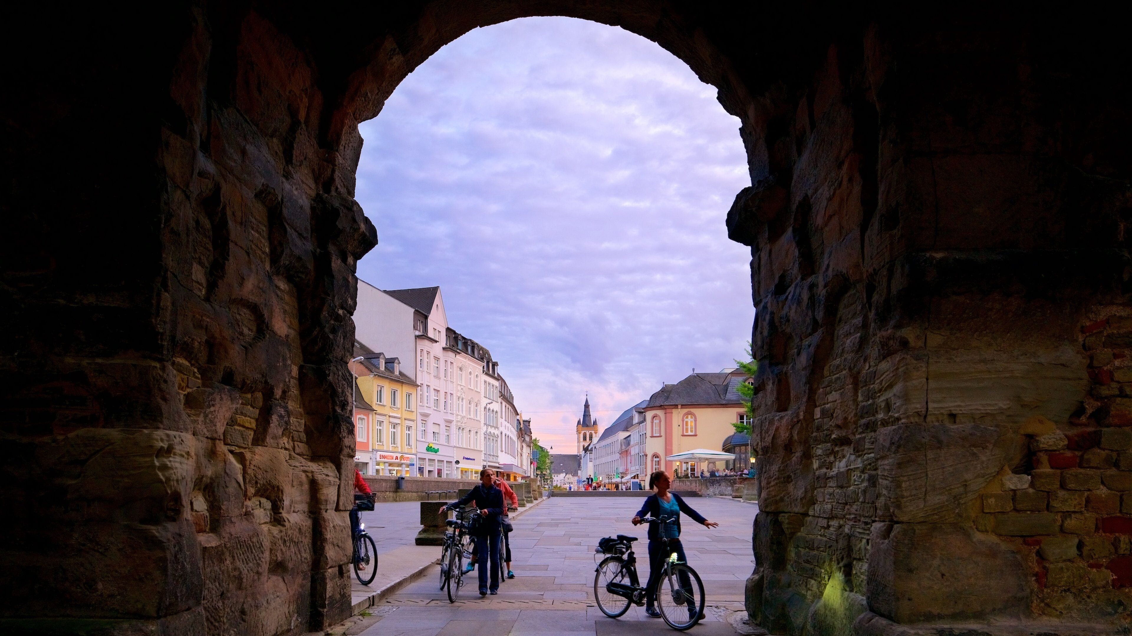 Porta Nigra featuring a sunset and a square or plaza as well as a small group of people
