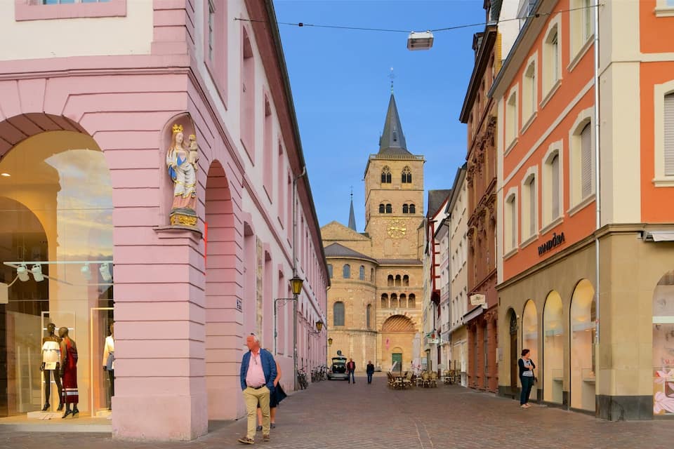 A street with pink and orange buildings, a church with a tall spire, and mannequins in a shop window.