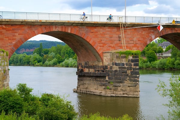 Eine Steinbrücke mit Bögen über einem Fluss, umgeben von Grün und Hügeln.