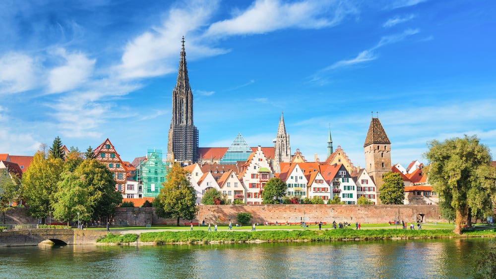A river with a bridge, historic buildings, and a tall cathedral spire.