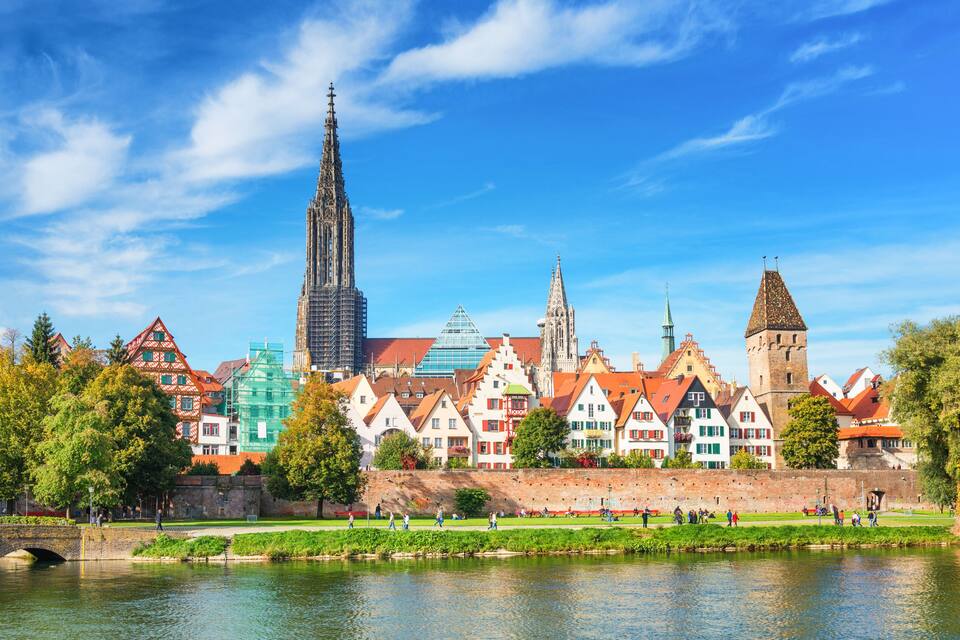A river with a bridge, historic buildings, and a tall cathedral spire.