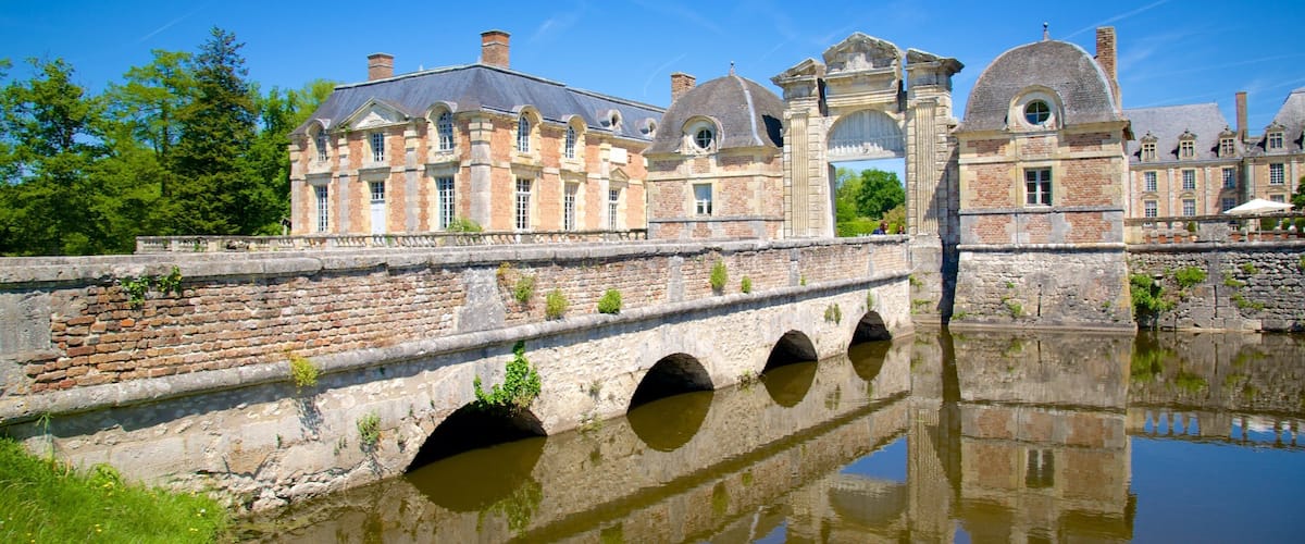 A historic stone bridge over a calm river with a reflection of a large building with arched windows and a dome.