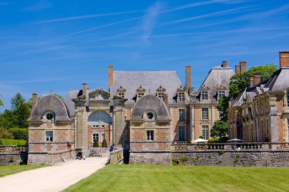 A historic building with multiple chimneys, a stone wall, and a pathway leading to the entrance.