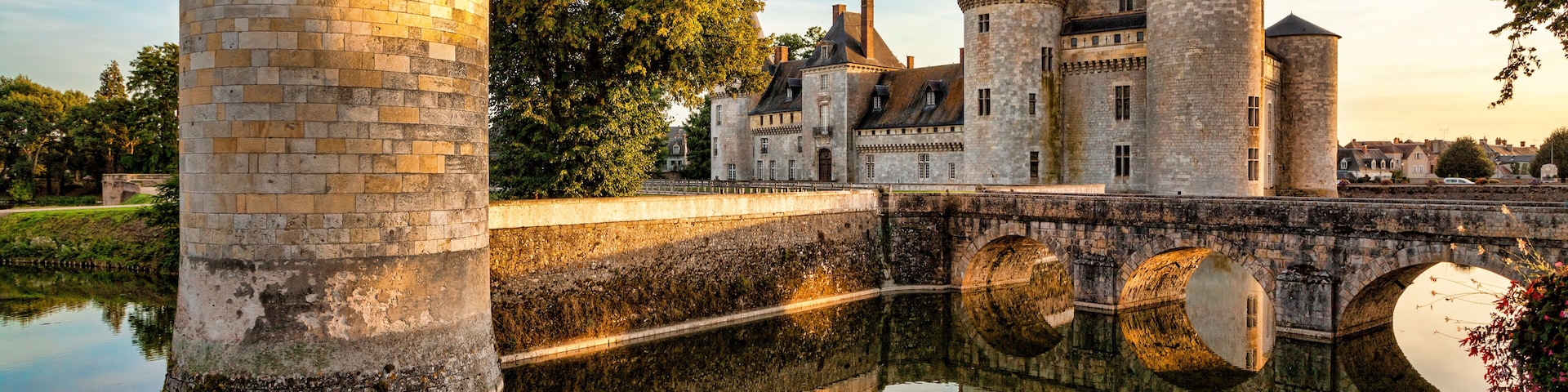 Un castillo histórico con múltiples torres, un foso y un puente que refleja la estructura.