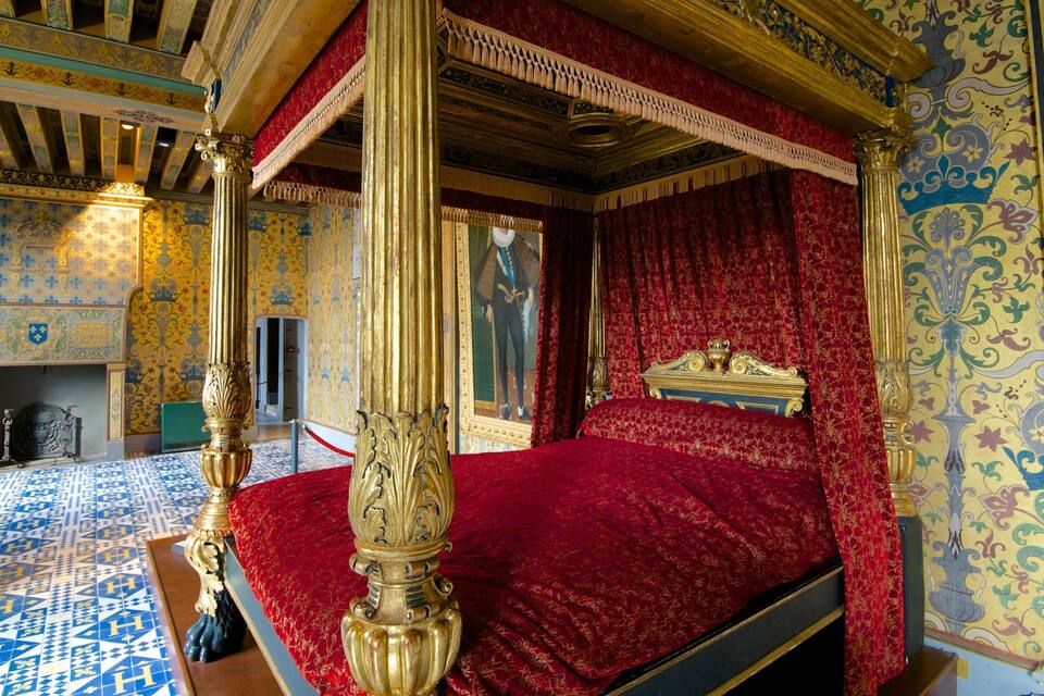 Een rijk gedecoreerde slaapkamer met een groot bed, versierde zuilen en behang met een patroon.